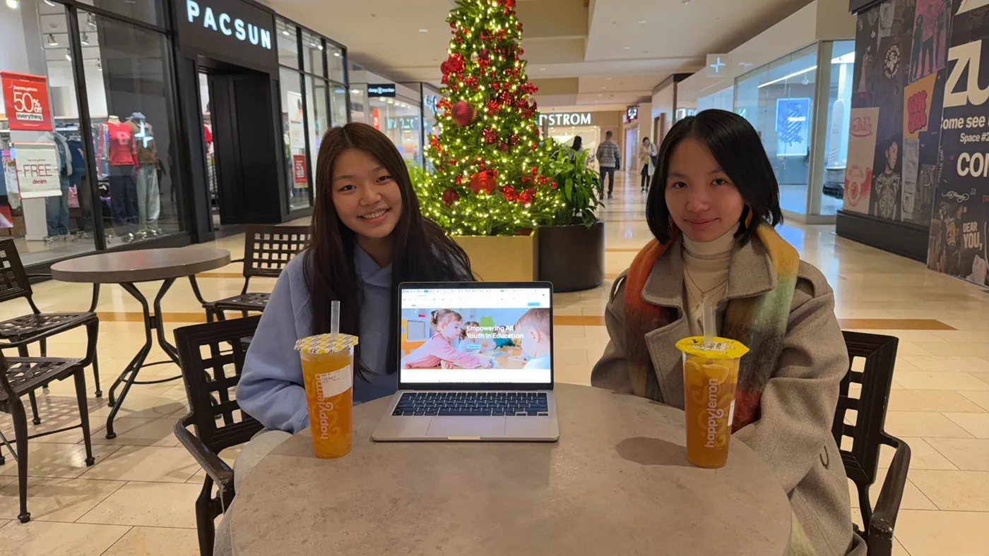 Two IncludEdU team members at a table with a laptop showing the website