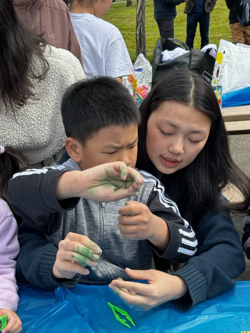 A volunteer helping a child with a hands-on craft at an outdoor community event