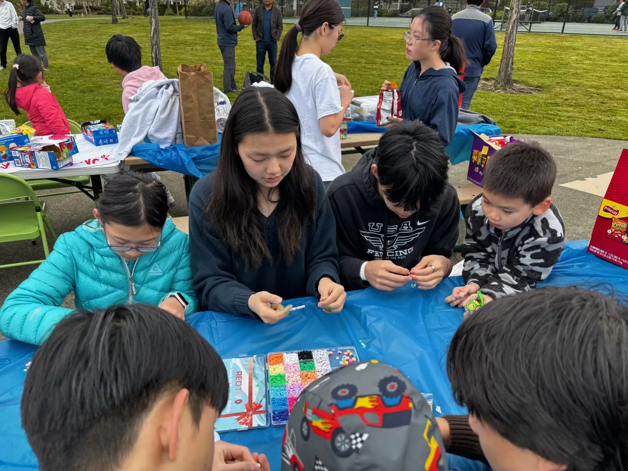Volunteers and children making bead bracelets together at an outdoor community event