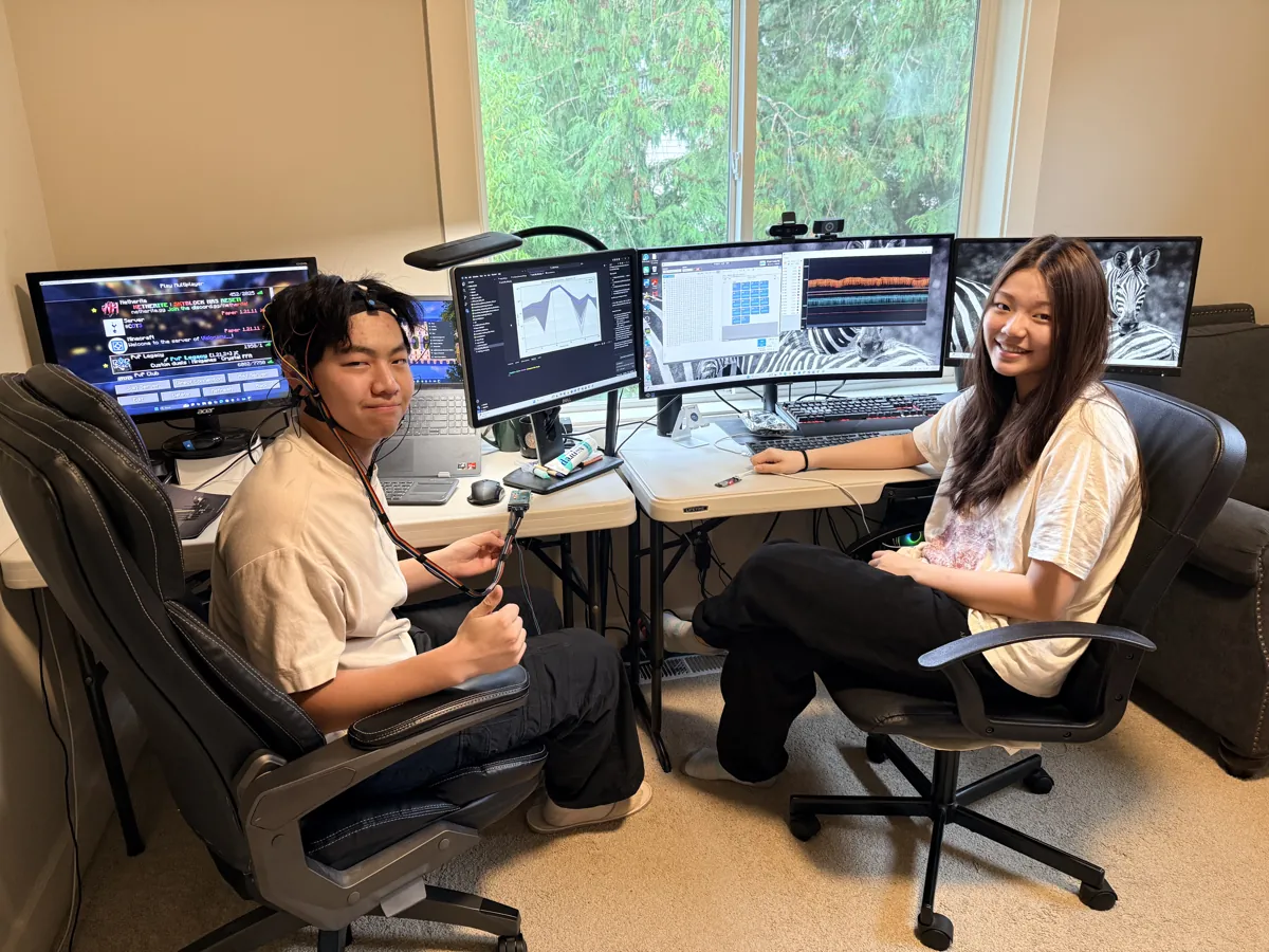 Two team members at a multi-monitor workstation, one wearing an EEG headset